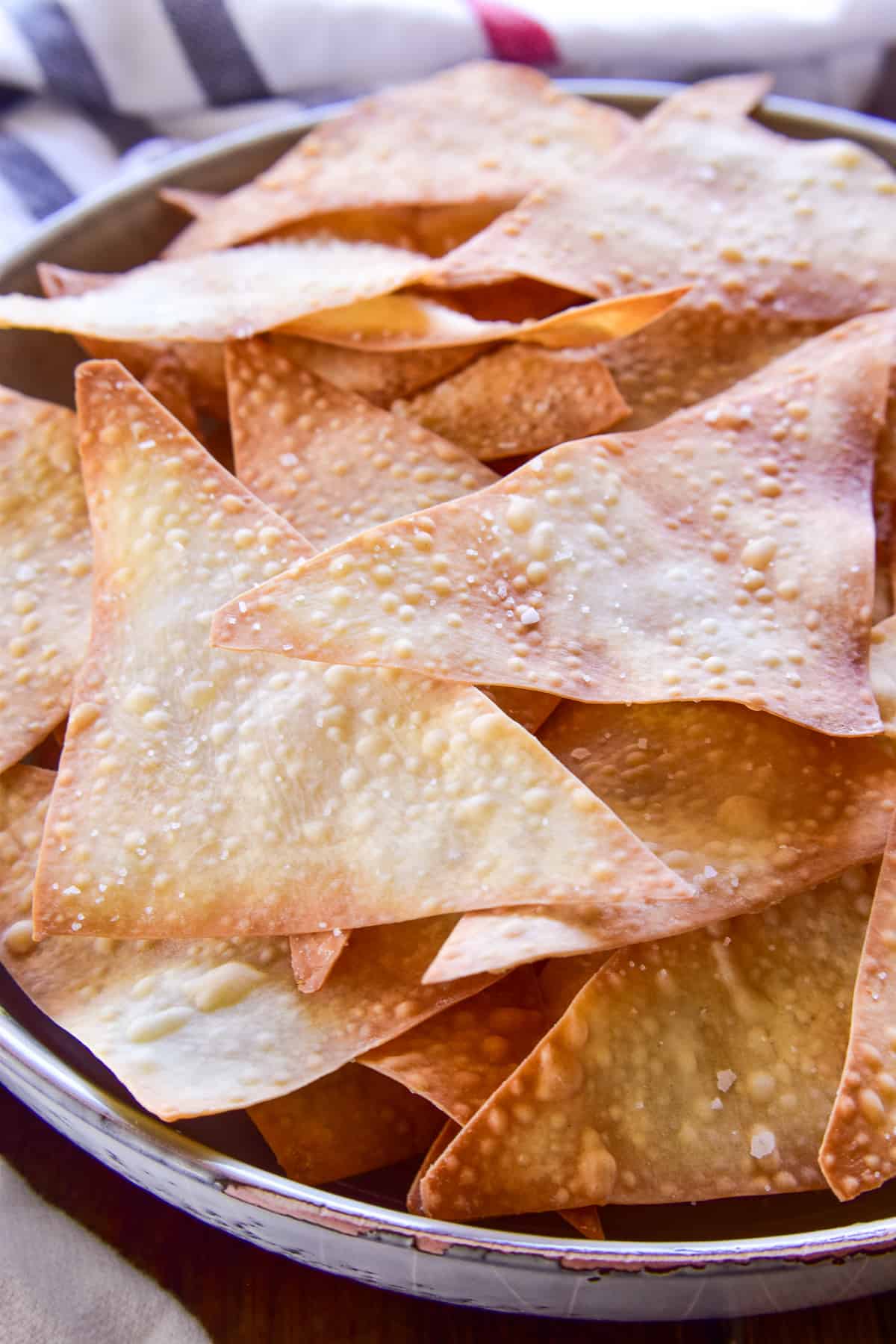 Side view of Wonton Chips in a gray bowl with a striped towel