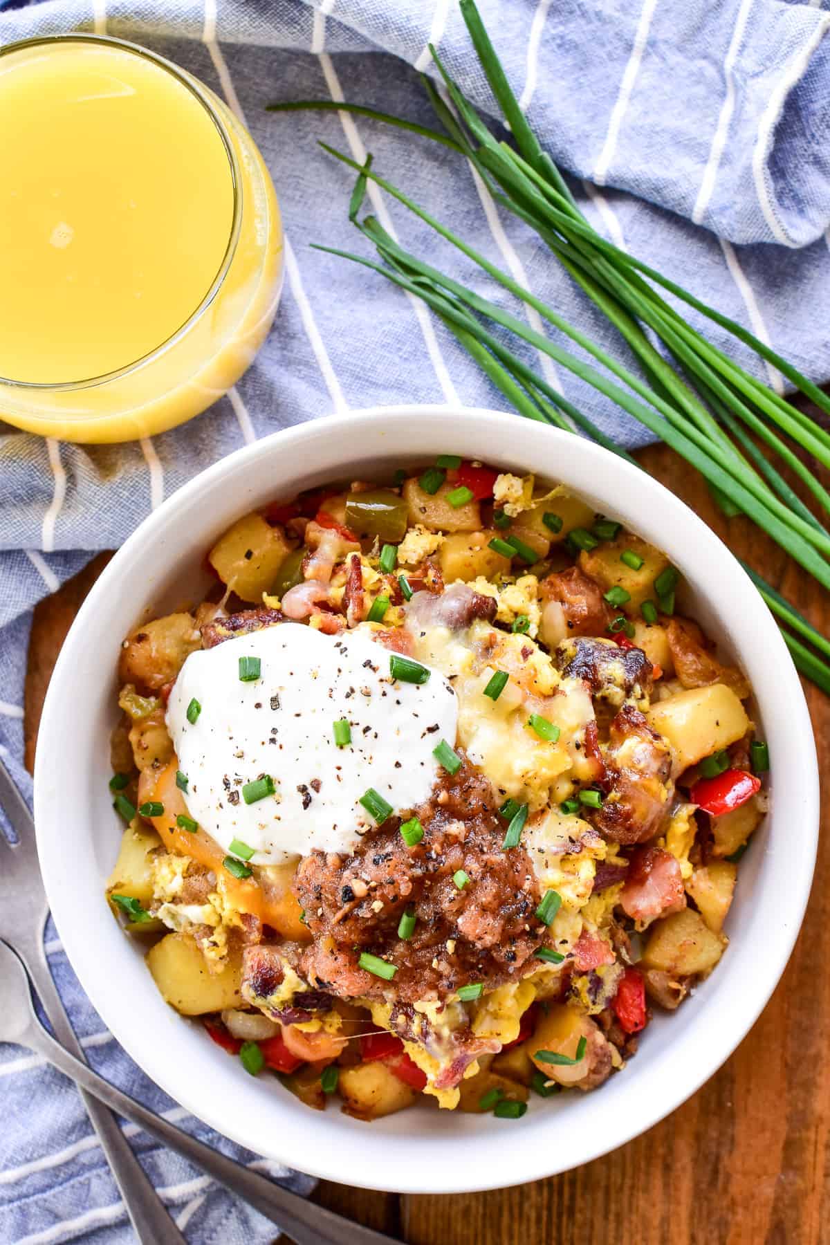 Overhead image of Breakfast Bowl topped with sour cream and salsa with orange juice, fresh chives, and a blue and white striped towel