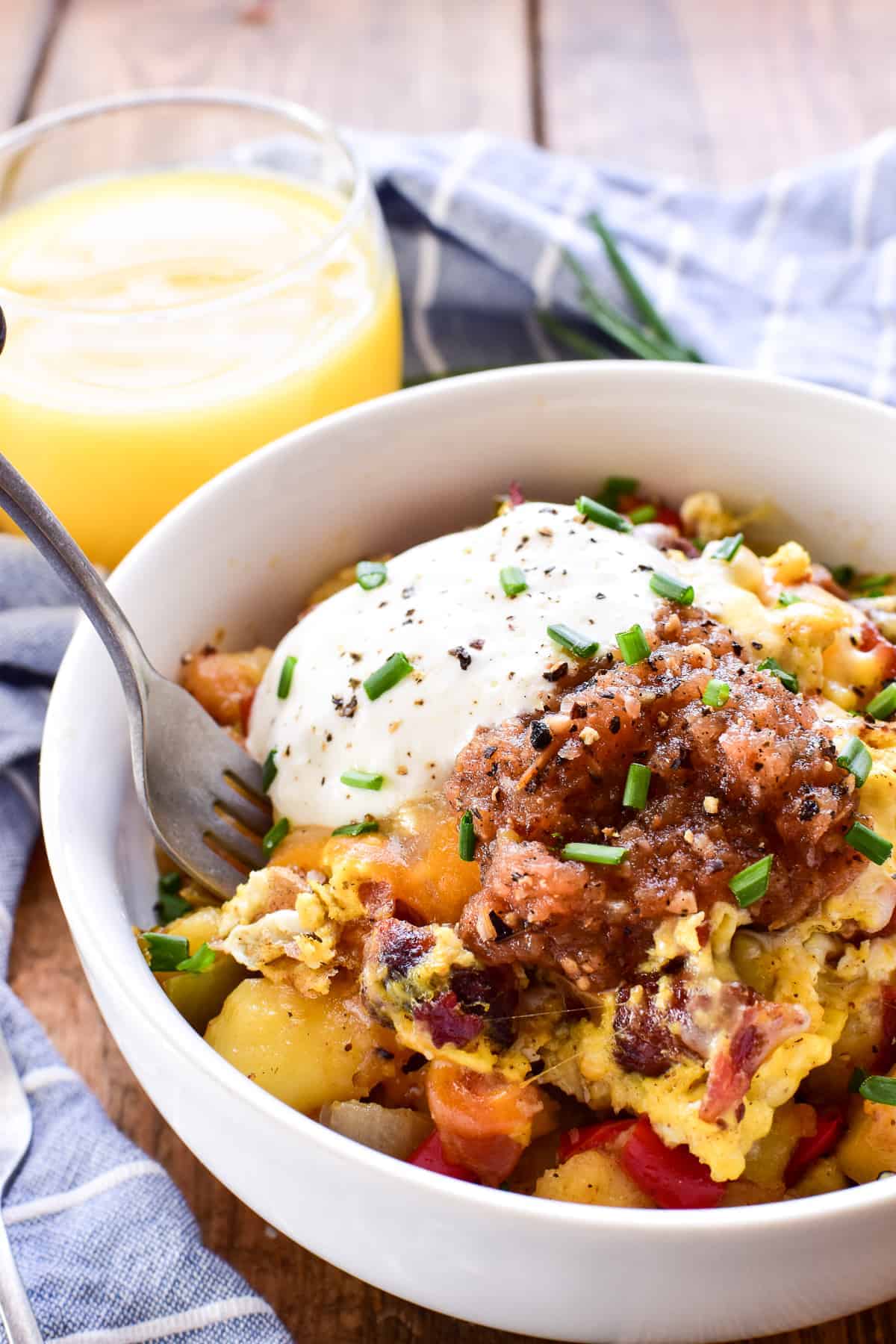 Breakfast Bowl in a white bowl with a fork, a blue and white striped towel and a glass of orange juice in the background