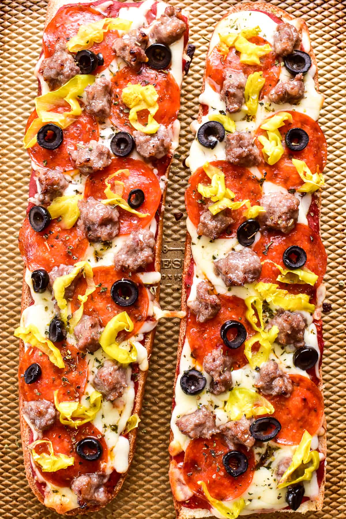 Overhead image of 2 French Bread Pizzas topped with sausage, pepperoni, black olives, and pepperoncini peppers