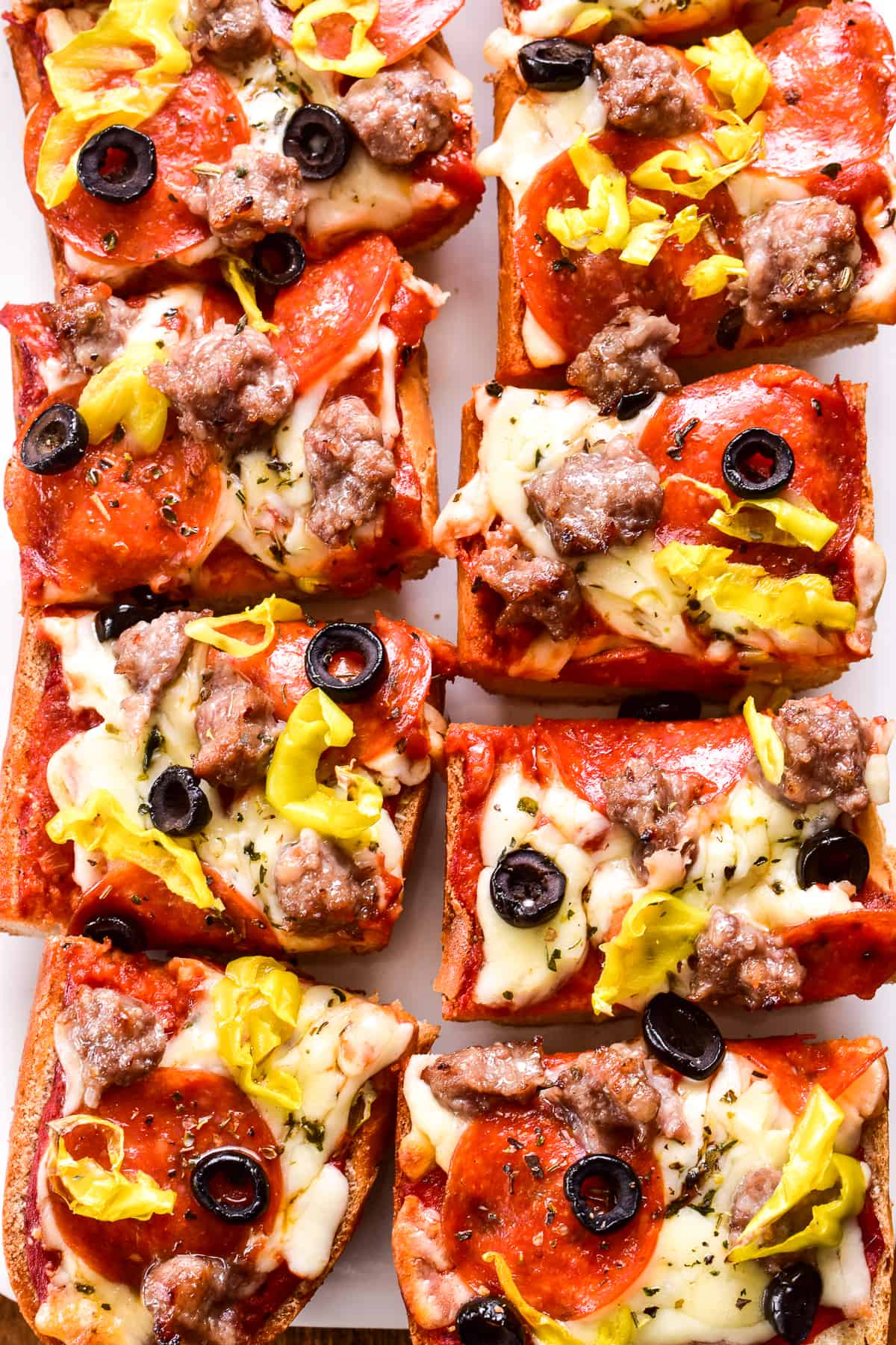 Overhead image of 8 pieces of French Bread Pizza topped with sausage, pepperoni, black olives, and pepperoncini peppers