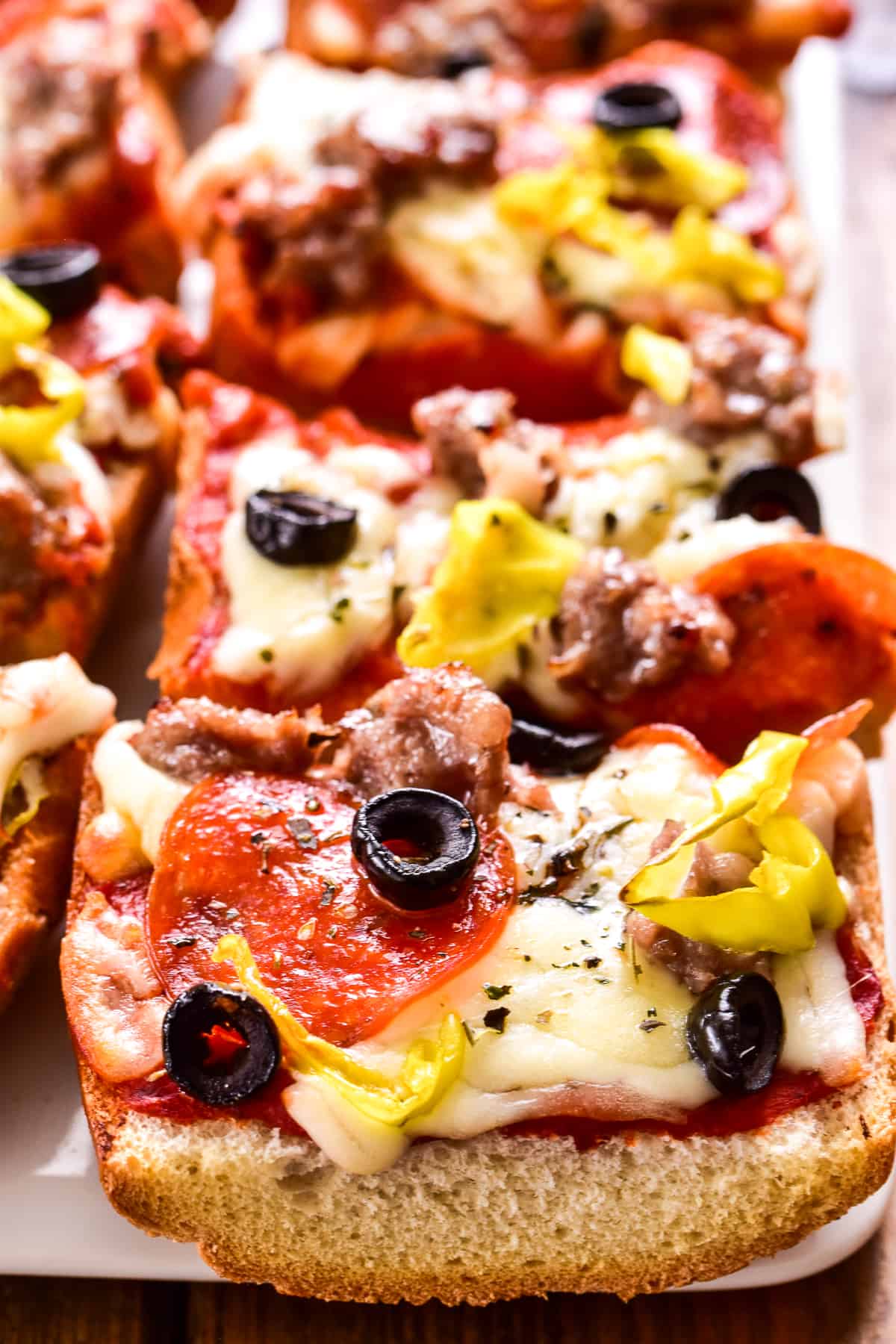 Close up of French Bread Pizza with sausage, pepperoni, black olives, and pepperoncini peppers